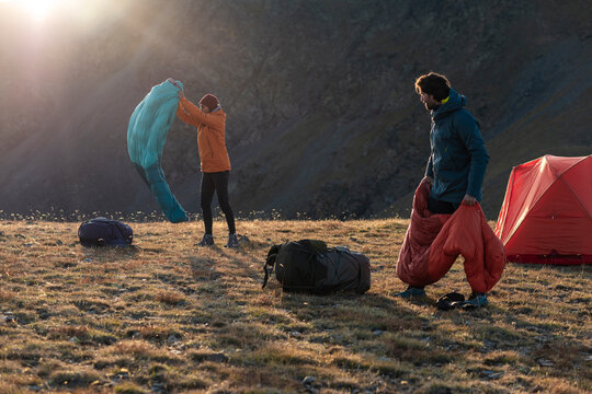 Backlit adventurous couple lifting sleeping bags in dramatic alpine light