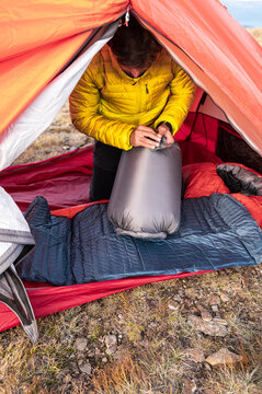 Focused camper inflating sleeping pad inside alpine tent