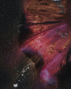 Aerial view of an abstract landscape with swirling patterns of crimson and umber hues, punctuated by stark white patches, Highland, Iceland.
