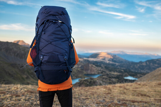 Lone adventurer carrying heavy backpack above mountain valleys