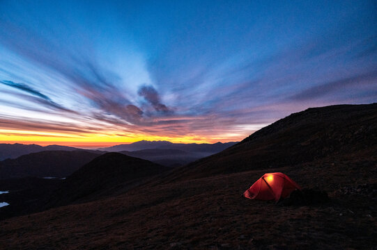 Lonely tent illuminated during dramatic twilight in high mountains