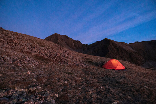Remote tent resting on rocky slope under twilight mountain sky