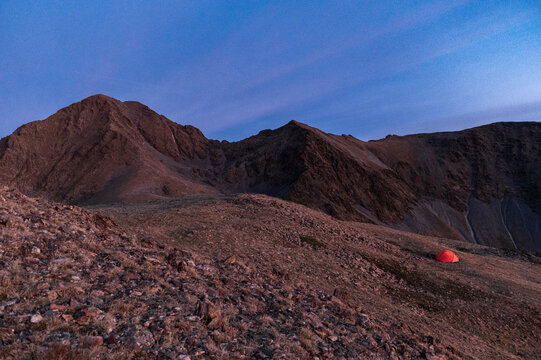 Lonely campsite positioned beneath rugged alpine ridgeline at dusk