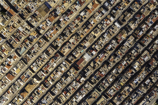 Aerial view of tightly packed buildings with warm terracotta roofs casting long shadows along narrow streets, Avola, Syracuse, Italy.