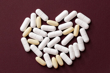 White and yellow pills arranged in heart shape. Capsules on red background. Medicine and healthcare concept. Pharmaceutical supplements composition. Love and health symbolism.