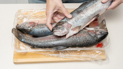 Freshly caught trout being handled by a person in a kitchen setting, with a wooden cutting board...