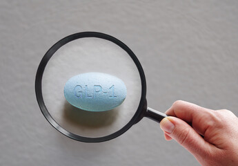 A hand holding a magnifying glass over a  GLP1 pill