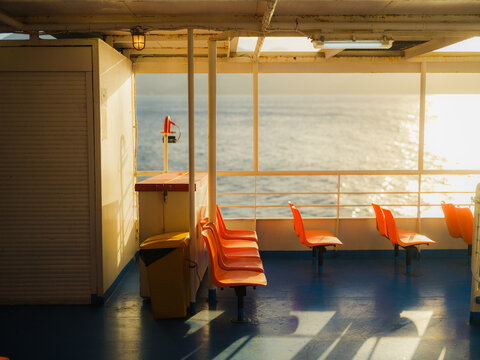 Plastic chairs on deck of a ferry lit by sunlight 