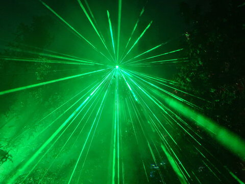 green laser light in a forest with many beams in the dark sky 