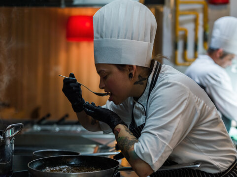Chef Tasting Dish in Busy Kitchen During Evening Preparation