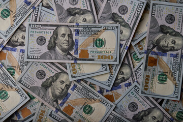 A close-up view of scattered 100-dollar bills featuring Benjamin Franklin&rsquo;s portrait