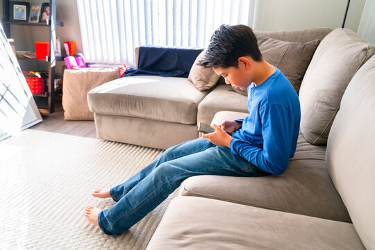 Boy Sitting on a Couch Using a Smartphone in a Living Room