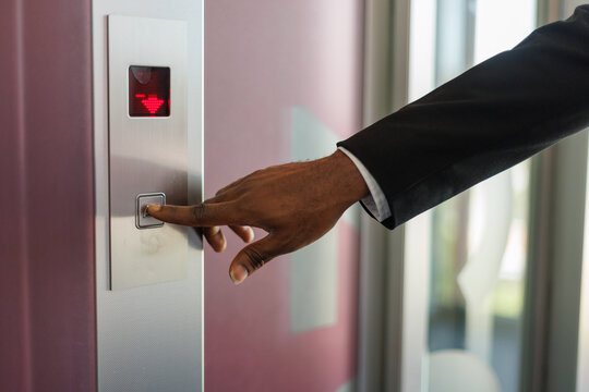 Partial view of hand of businessman pushing button in blurred elevator