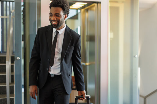 Young smiling male entrepreneur going with suitcase in hotel hall