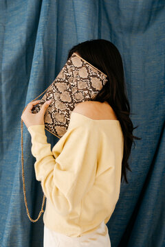 Woman hiding face with snakeskin clutch purse
