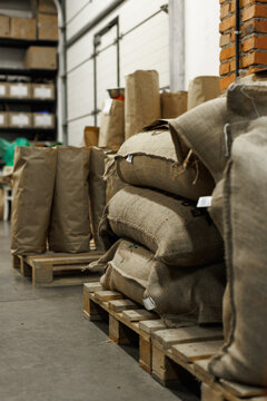 Sacks with coffee beans on wooden pallet at warehouse of food factory