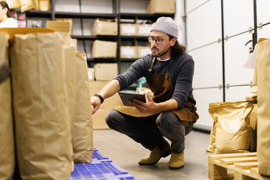 Male worker with digital tablet checking packages with coffee beans