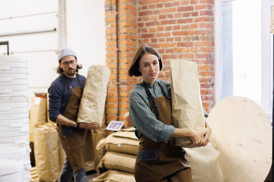 Workers carrying packages with coffee beans at warehouse of factory