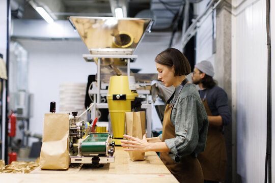 Female worker packing package with coffee beans near male colleague