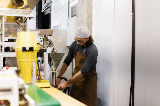 Young male worker controlling how coffee beans falling out in package