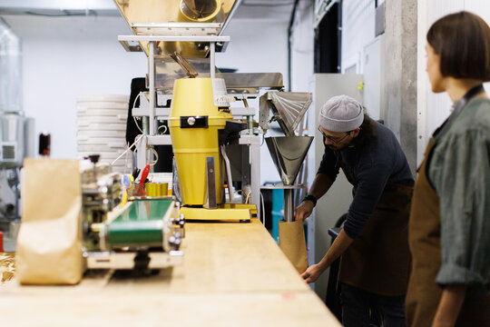 Worker looking at man controlling coffee beans falling out in package