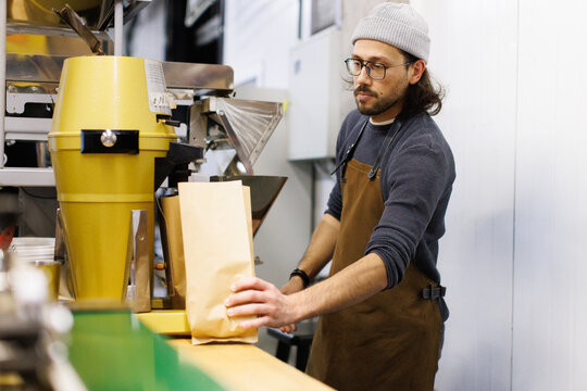 Young male worker putting package with coffee beans on table