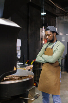 Concentrated black male worker controlling process of coffee roasting