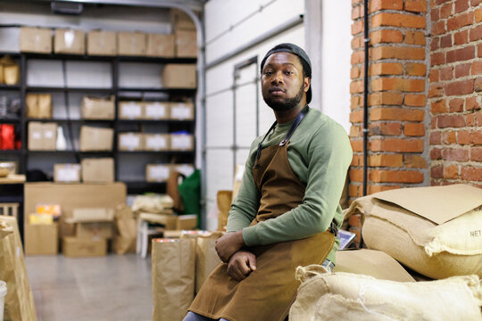 Portrait of young black male worker sitting on sacks with coffee