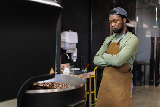 Young focused black male worker controlling process of coffee roasting