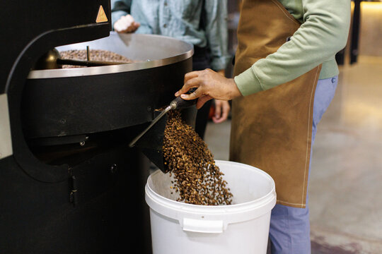 Cropped workers controlling of coffee beans falling out in bucket