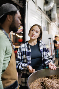 Young workers controlling process of coffee roasting at factory