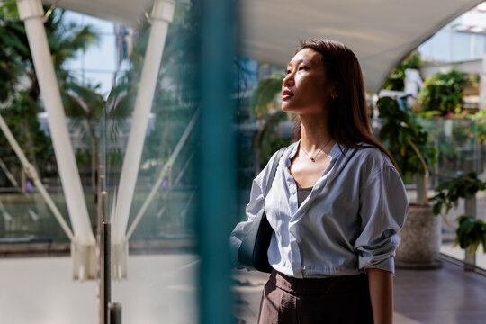 Woman gazes upward in sunlit atrium, reflecting on future.