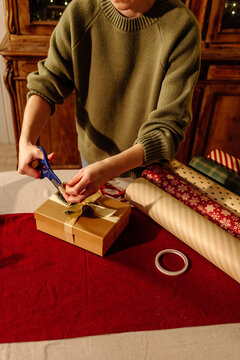Person Wrapping Christmas Gift Box with Ribbon and Decorative Elements