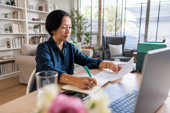 Woman works from home, reviewing documents and taking notes.