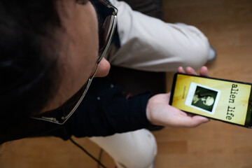 Person Holding Smartphone with Alien Life and UFO Disclosure Content, Top Down View of Mobile Screen Showing Grey Alien Photo Research