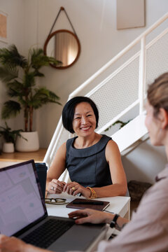 Two women meet at a table with a laptop.