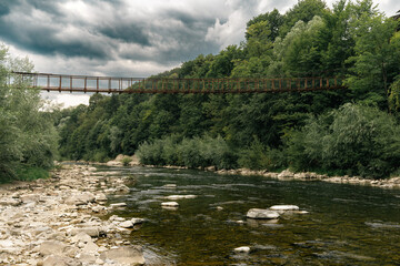Fototapeta premium Suspension Bridge Over Mountain River in Forest Landscape