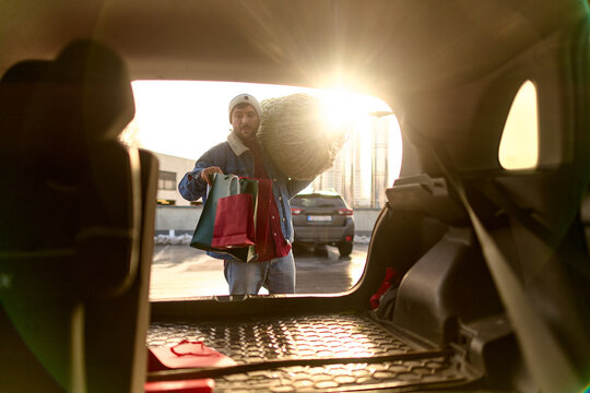 Man Loading Christmas Tree and Shopping Bags into Car Trunk