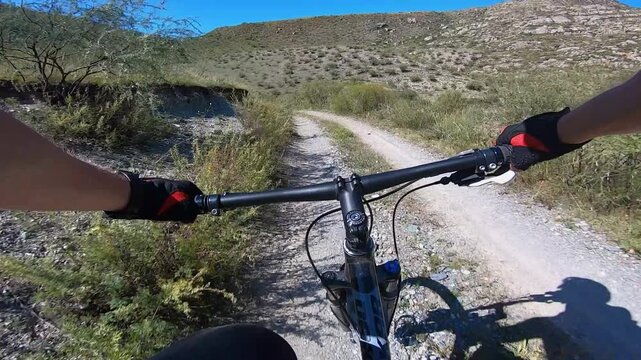 First Person Cyclist Following Teammate Across Dirt Gate, Open Hillside Track, Passing Rusty Farm Gate, Dusty Gravel, Pacing Behind Another Rider, Tactical Overtaking And Steady Cadence, Countryside