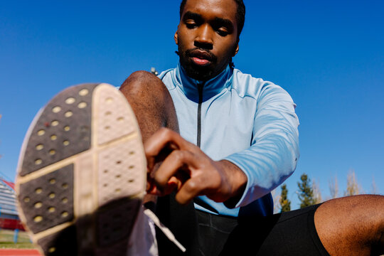 A runner seated on the track fastening his athletic shoes