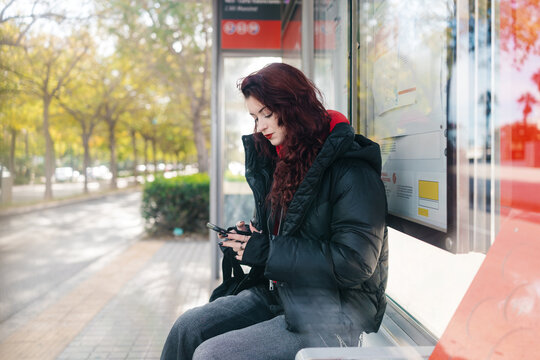 Young woman waiting at bus stop checking phone