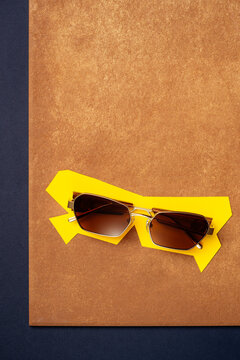Sunglasses on geometric yellow paper cutout on textured terracotta