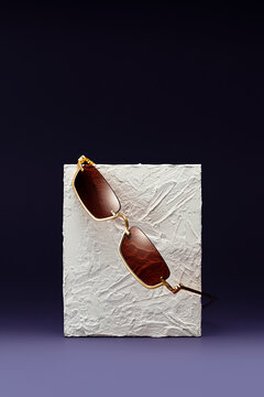 Sunglasses hanging on a concrete block on purple and black background