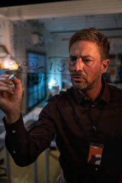 Man writes equations on glass, deep in thought.