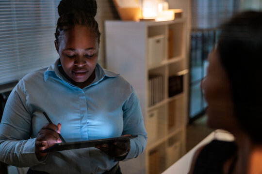 Woman using tablet in dimly lit office setting.
