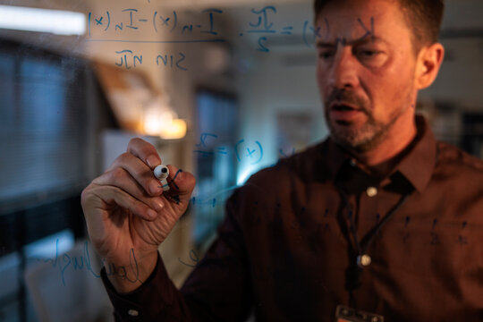 Man writes complex math equations on glass board.