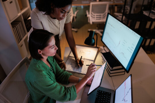 Two women analyze financial data on multiple screens.