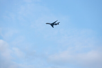Fototapeta premium Airplane flying in a clear blue sky with scattered clouds, showcasing its wings and fuselage in a high-altitude perspective against a serene backdrop