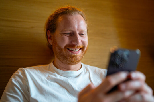 Man smiles while using his phone in indoor setting
