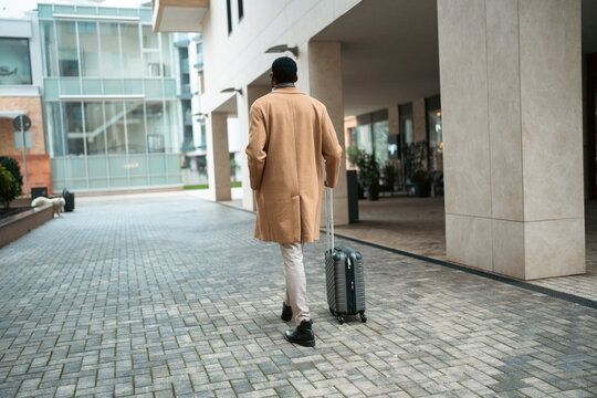 Man walks with suitcase through city street
